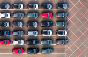 An aerial view directly above rows of newly built cars in the automobile industry on a commercial dock ready to be loaded for export and import with VAT and tariffs