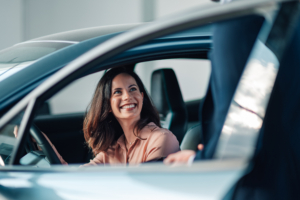 Happy woman sitting inside a new car at a dealership, smiling during the buying process with a salesperson